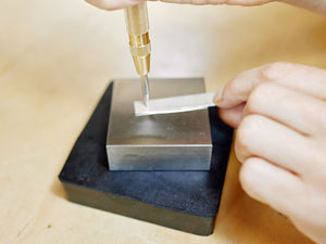 Person using an automatic centre punch on a metal block with a blurred background | Affordable Jewellery Making Supplies