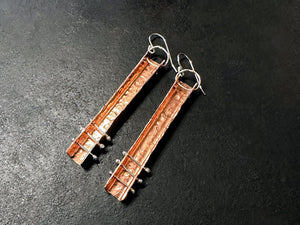 Pair of earrings with copper and sterling silver design on a dark surface | jewellery Course Melbourne