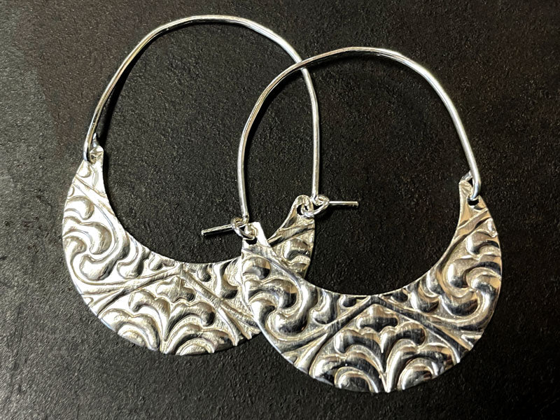 Silver hoop earrings with intricate patterns on a dark background | au jewelry