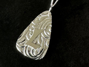 Silver pendant with intricate design and letter 'L' on a black background | Jewellery Making Courses