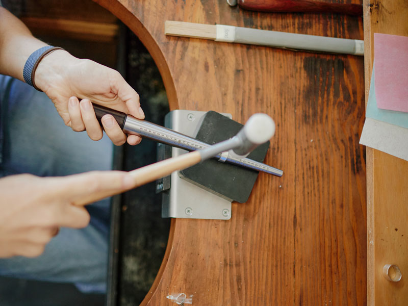 Person using a hammer to hammer a silver ring on a mandrel on a wooden surface |