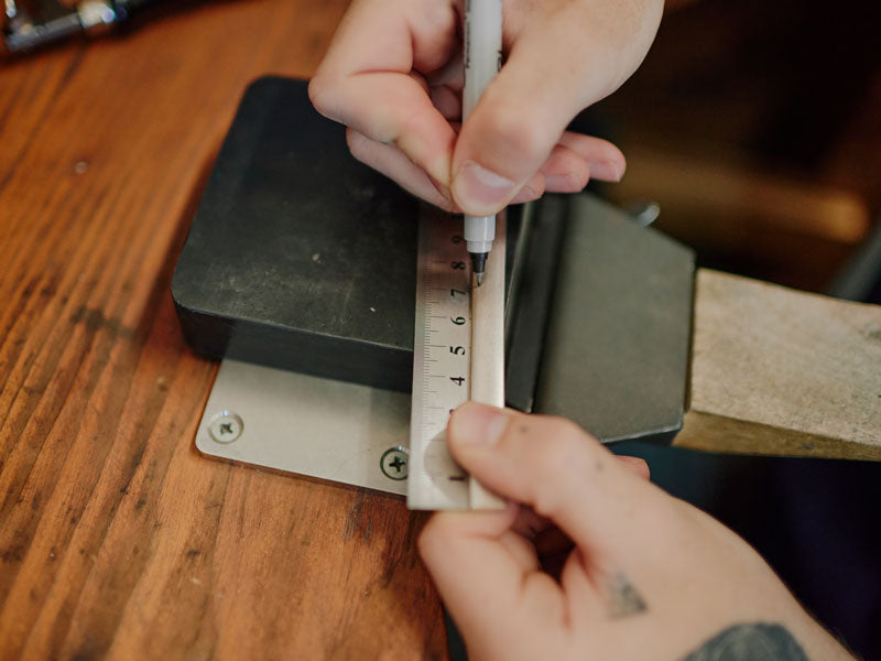 Person measuring a piece of sterling silver with a ruler on a wooden surface | Jewellery Supplies Sydney