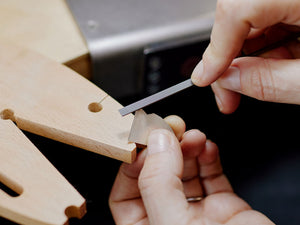 Person using a needle file on a pieces of silver while resting on a wooden bench peg with a blurred background | Jewellery tools Australia