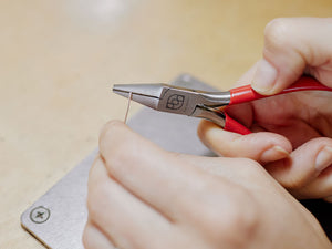 Close-up of hands using a pair of chain-nose pliers on a light-colored surface | jewelry pliers