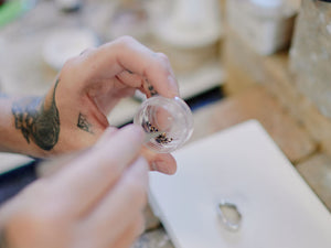 Hand holding a small transparent container with pallions of silver solder, blurred background | soldering tools