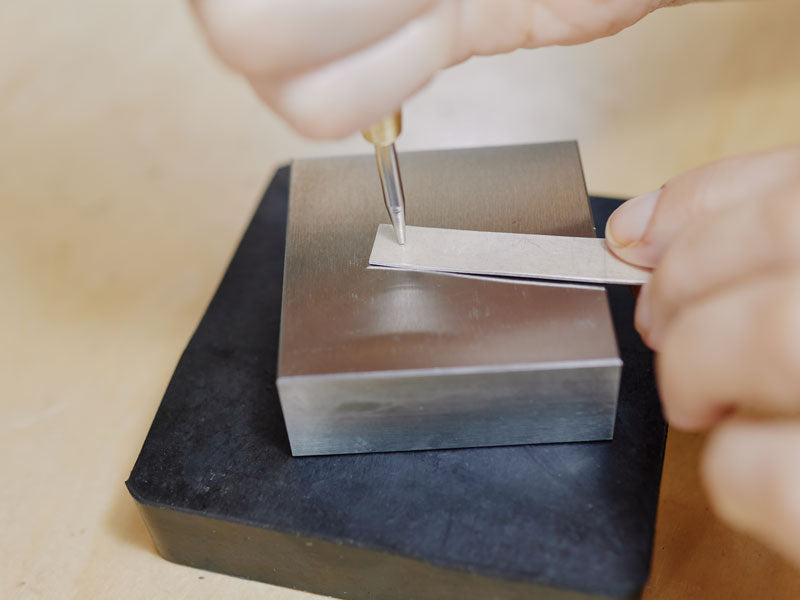 Person using an automatic centre punch on a metal block with a blurred background | Jewellery Tools
