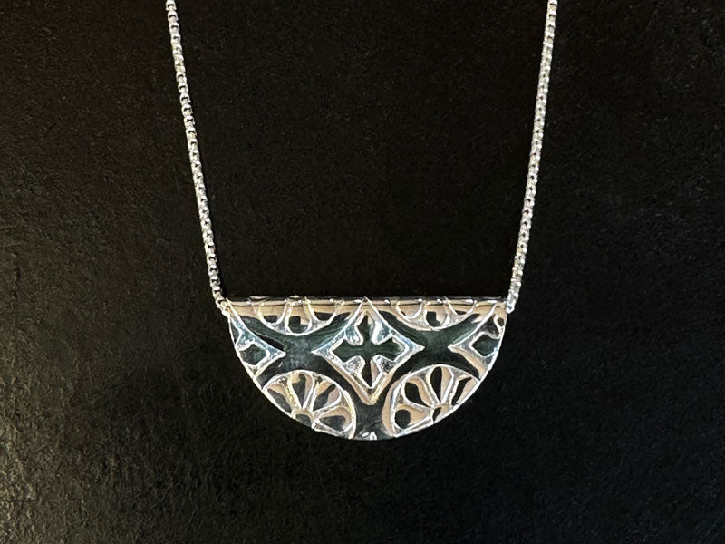 Silver necklace with a half-circle pendant on a black background | Jewellery Design Course