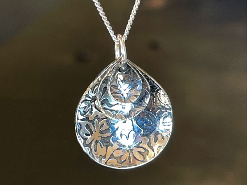 Silver pendant with floral patterns on a chain against a dark background | jewelry supplies Australi