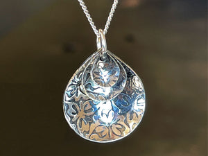 Silver pendant with floral patterns on a chain against a dark background | jewelry supplies Australi