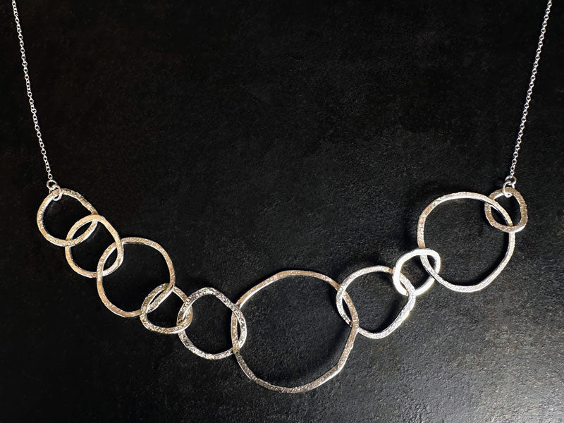 Silver necklace with interlocking rings on a black background | jewellery lessons