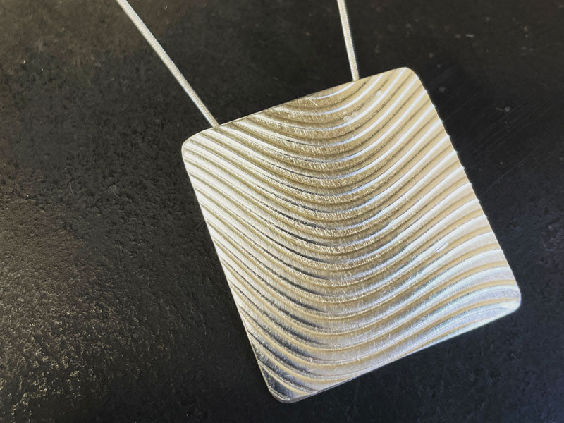 Embossed silver pendant on a black background | Metal texturing techniques