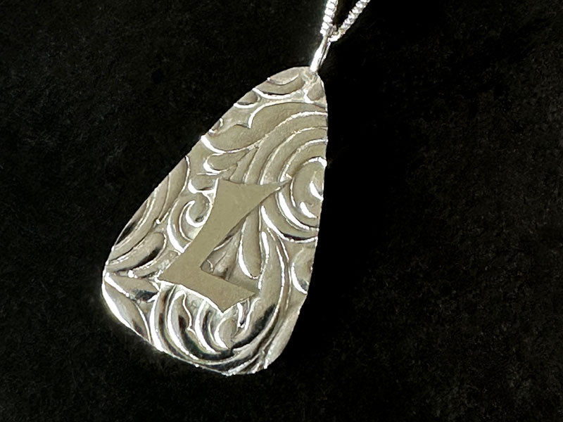 Silver pendant with intricate design and letter 'L' on a black background | Jewellery Making Courses