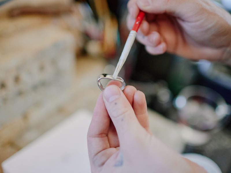 Person holding a silver ring and painting flux with a paint brush | soldering flux