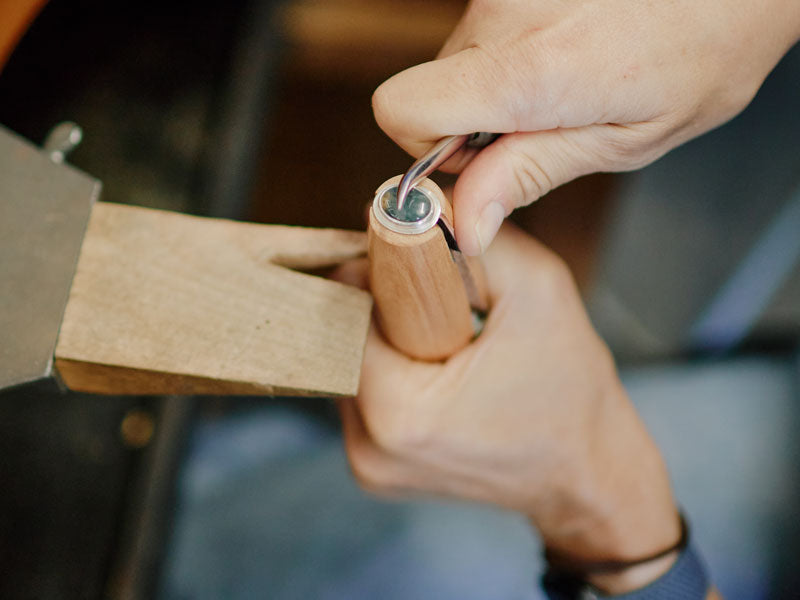 Person setting a ring in a wooden ring clamp on a wooden bench pin with a blurred background | Australian Jewellery Supplies