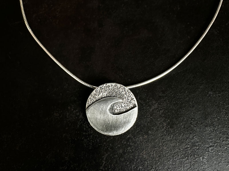 Silver necklace with a sandstone hammer textured wave pendant on a black background | Australian Hammer Supplies